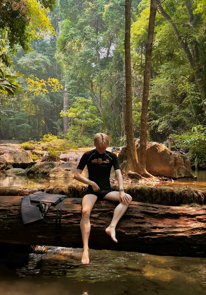 Zino Barbe zittend op een boomstam boven een rivier in het bos